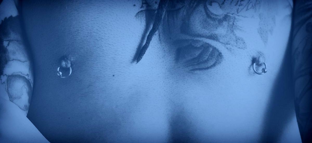 Man with pierced nipples, chest tattoo, and PainfulPleasures blue overlay