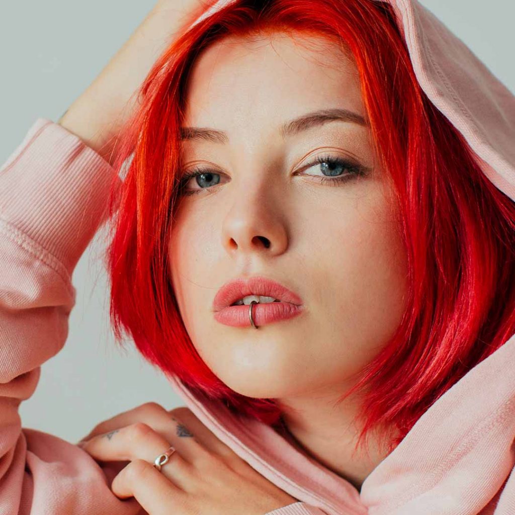 Girl with red hair and lip piercing wearing a pink hoodie