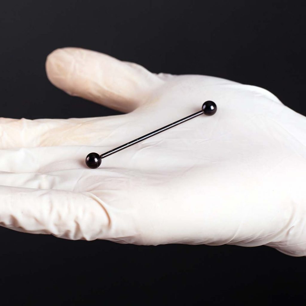 Black Industrial barbell in a gloved piercer's hand