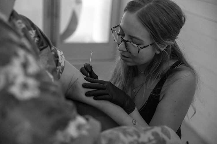 female tattoo artist giving a client a single needle stick and poke tattoo on arm