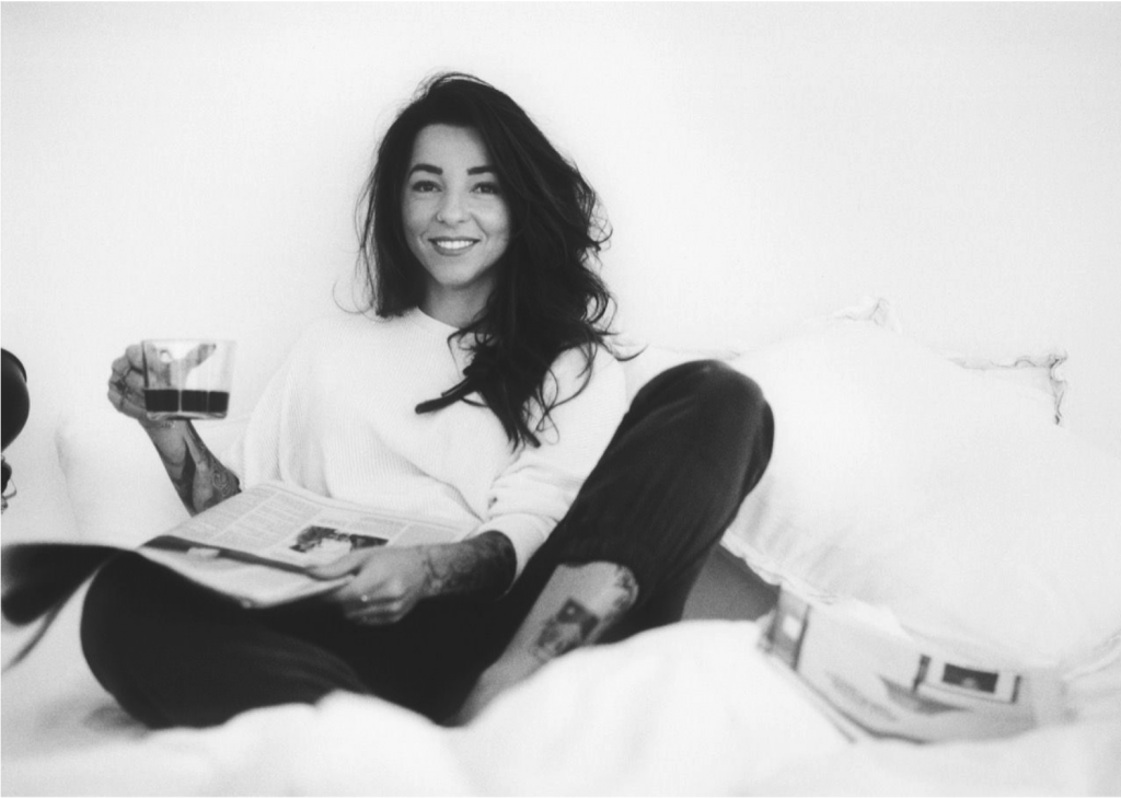 Black and white photo of tattoo artist Trudy Lines reading a magazine and holding a glass pot of coffee