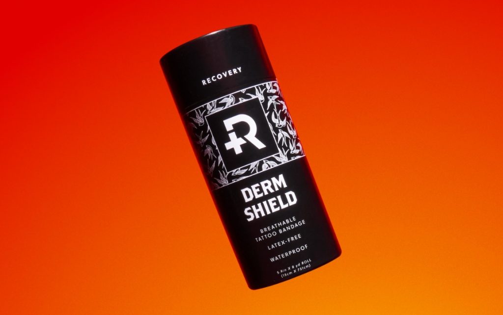 Roll of Recovery Derm Shield tattoo aftercare bandage in full black packaging with Recovery logo on the front. The image appears over an orange backdrop.