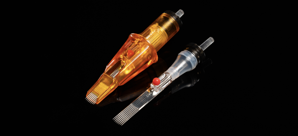 Photo of Peak Triton cartridge tattoo needles, showing one with the orange casing, and one without