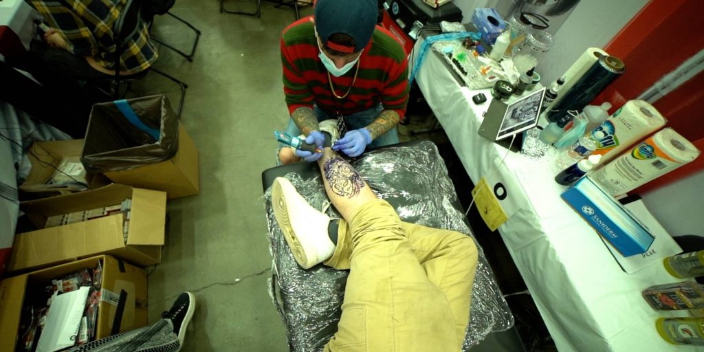 Aerial view of tattoo artist outlining a tattoo on a client's thigh