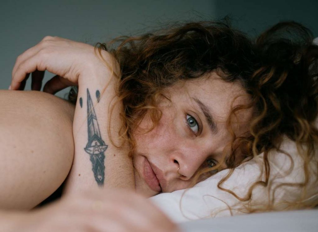 Tattooed woman lying in bed looking burnt out