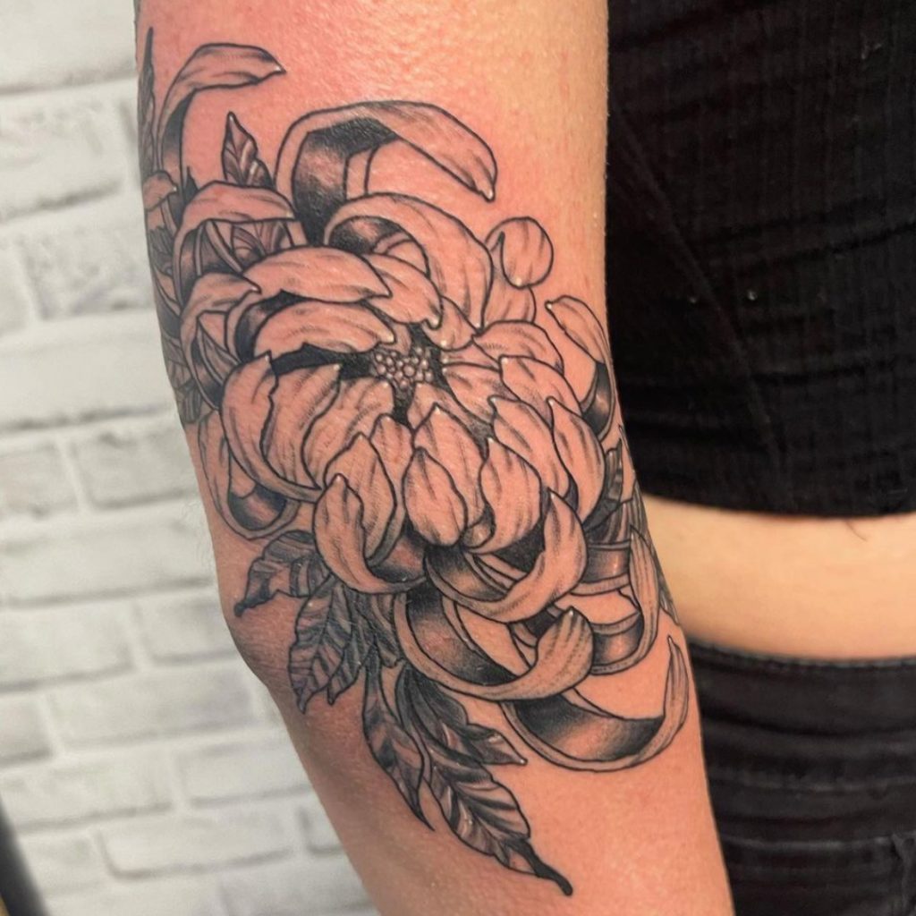 Tattoo client with hyperrealistic black and gray flower tattoo on elbow