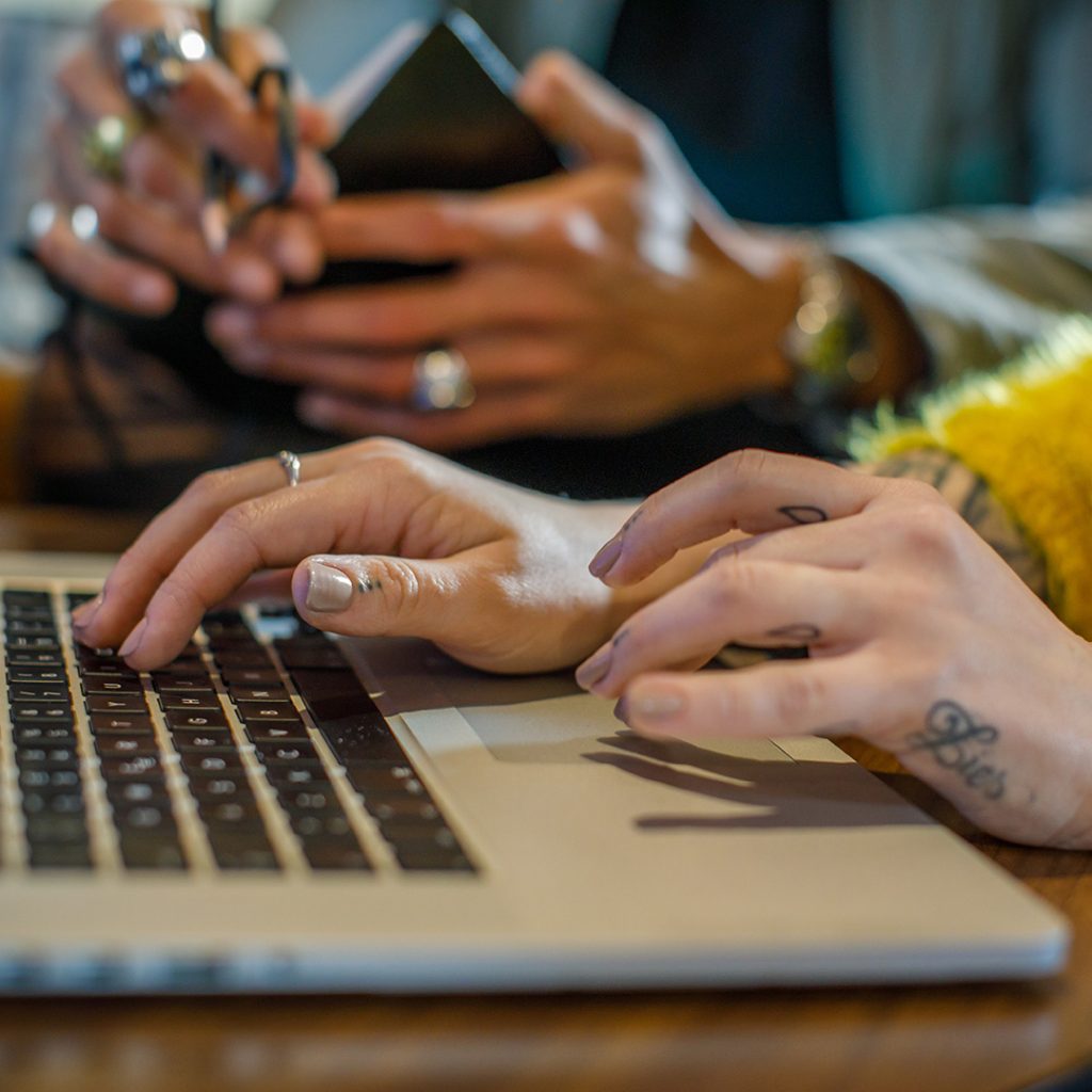 Tattooed hands typing on a laptop
