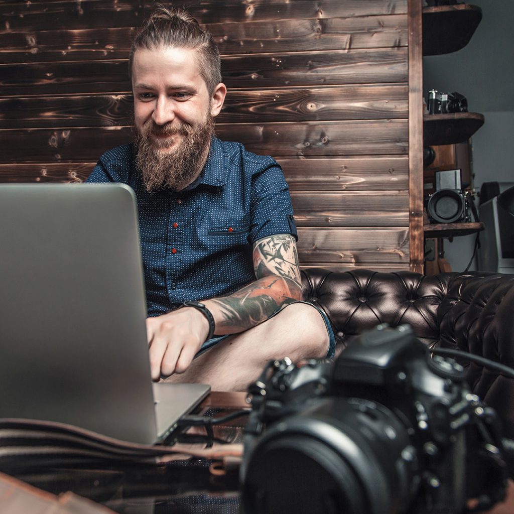 Tattoo artist in a blue button-down with full-sleeve tattoos using a laptop