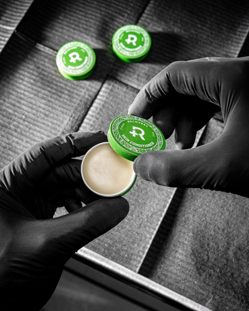 Gloved tattoo artist hands opening a small container of salve