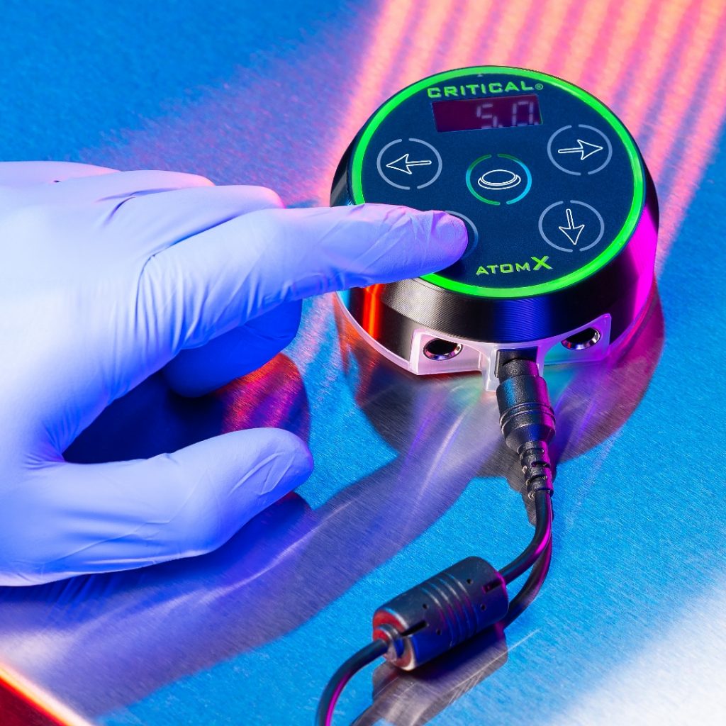 Tattoo artist's gloved hand toggling the voltage on a Critical power supply