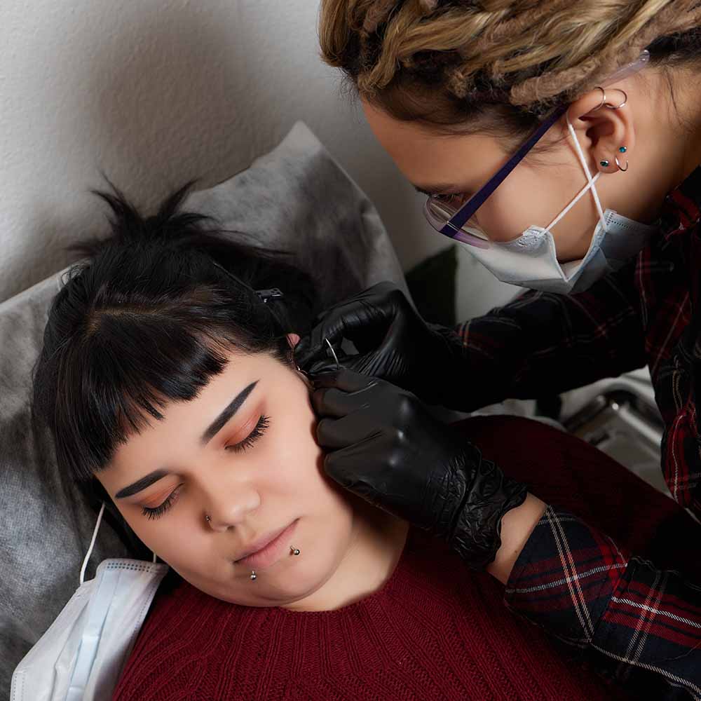 Client getting an ear piercing from a piercer wearing a face mask