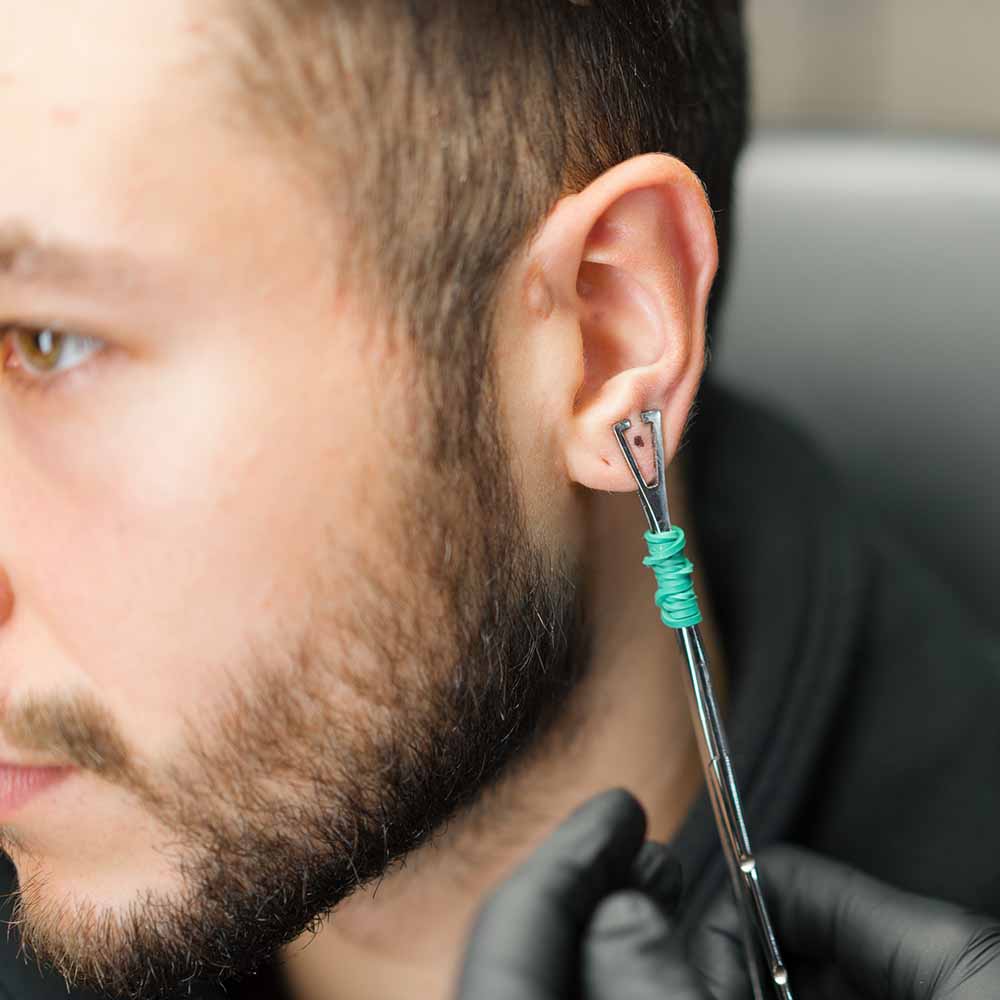 Client getting a stretched lobe piercing from a piercer using forceps